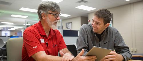 A middle school science education programstudent looks at an iPad with a professor in the EDvolution Center.  
