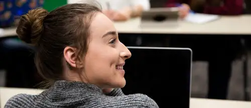 master of education administration missouri student smiles while looking up from her computer to listen to a lecture