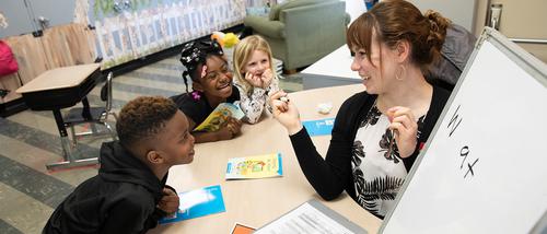 Early childhood education student in missouri teacher working on reading skills with a group of three students near a whiteboard. 
