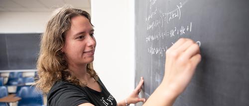 middle school math degree Student-teacher in the secondary math education program stands at the front of the class doing math on a chalkboard for her students 