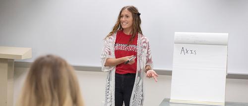 A student teacher stands by a large paper note pad teaching social studies to her classroom. 