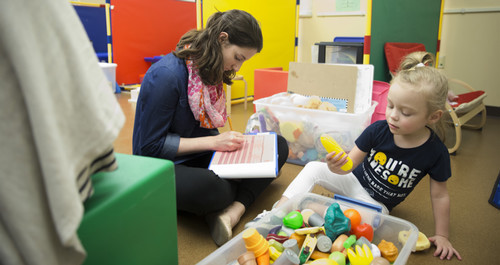 A child development major takes notes while observing a child playing with toys in a program classroom