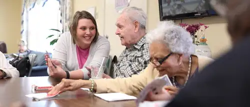 A family studies degree student sits and plays cards with residents at the family studies hoover center