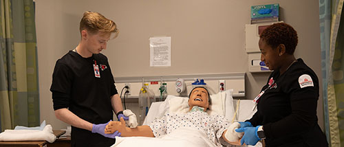 a Missouri nursing program student listens to an instructor as they prepare to practice a technique on a lab mannequin