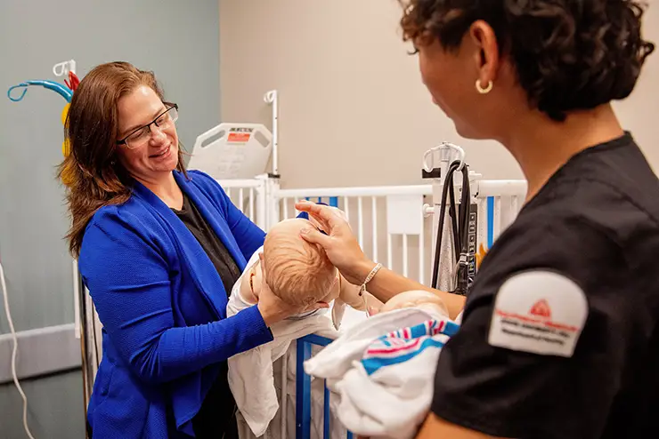 a nursing instructor works with a student on a manikin during class