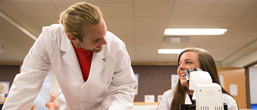 Students in the MLS Degree Science share a laugh during lab while doing work with a microscope. 