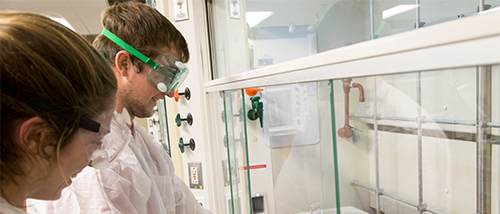 Southeast Missouri State University chemistry students smile while filling a beaker with a chemical. 