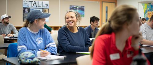 Students laugh with each other while sitting at their desks during a lecture session pursuing their mathematics teacher degree.