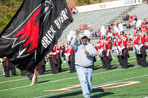 A man walking on the football field with a flag that says brick by brick