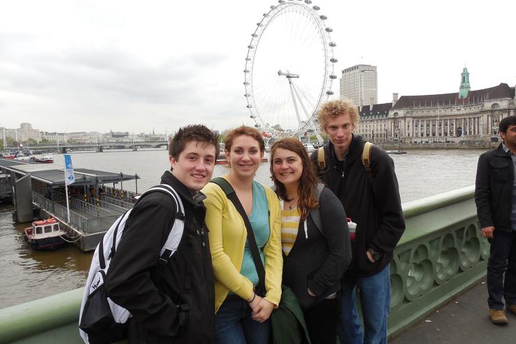 Four students wearing jackets pose in front of a large ferris wheel.