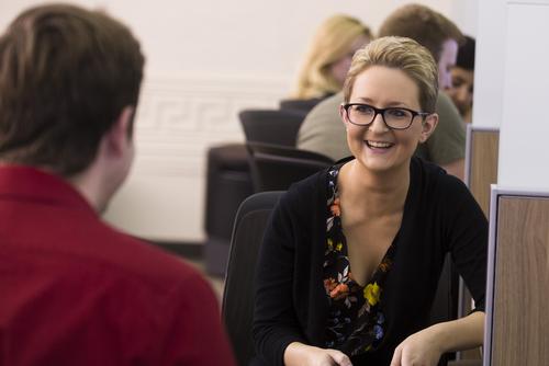 A woman, holding a calculator, meets with a learning assistant at Universal Tutorial Services. 
