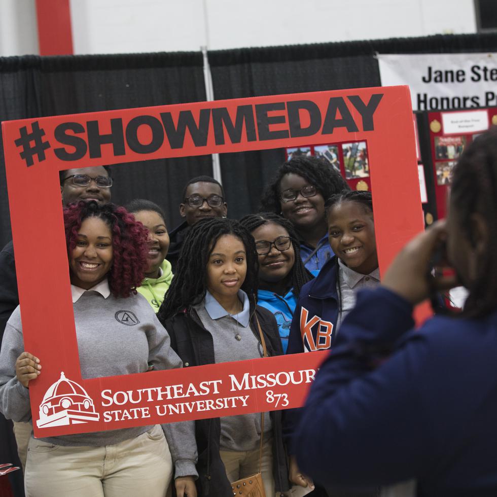Prospective students pose for a photo with a frame that reads “#SHOWMEDAY” 