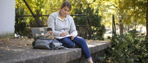 A student studies on her laptop on campus at semo, a test optional college in Missouri, with fall trees and sunshine in the background.