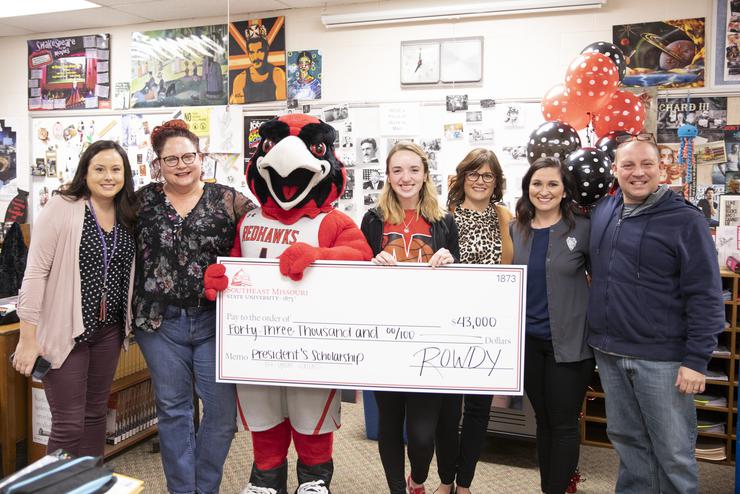 Southeast Missouri State University student receiving the President’s Scholarship during an award ceremony at their local highschool with a group of semo affiliates and family/supporters around them. 