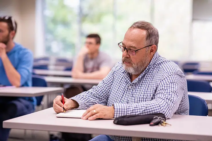 a older non-traditional adult student sits in a classroom and takes notes during lecture
