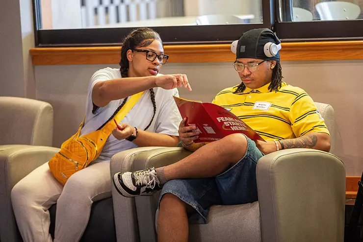 two students talk together going over the information in a booklet