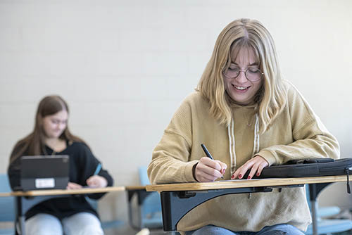 a young woman seated at a desk smiles as she does her classwork