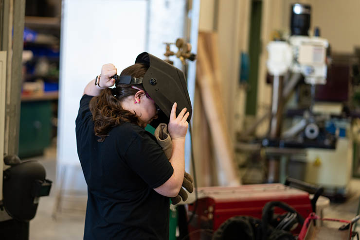 a young woman in a construction shop puts on a welding mask
