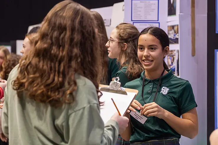 a regional high school student in her school uniform talks to a judge at the regional science fair
