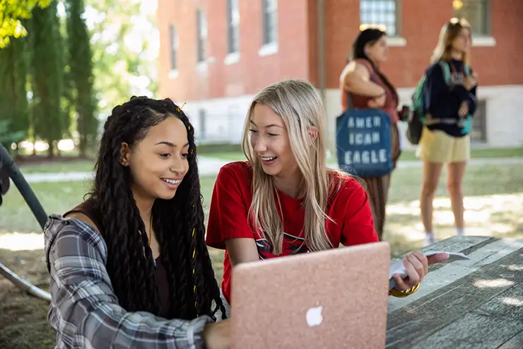two SEMO freshmen students sit together at a picnic table on the river campus with a computer between them