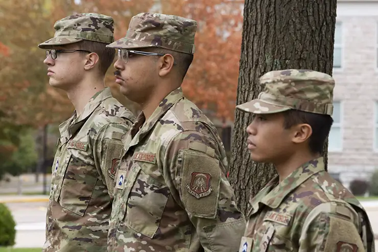 three young men in military uniform stand at attention for a ceremony