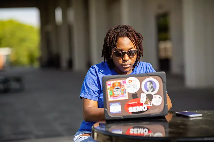 A SEMO online student sits on the kent library portico and works on her laptop