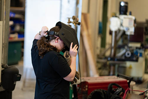 a young woman in a construction shop puts on a welding mask