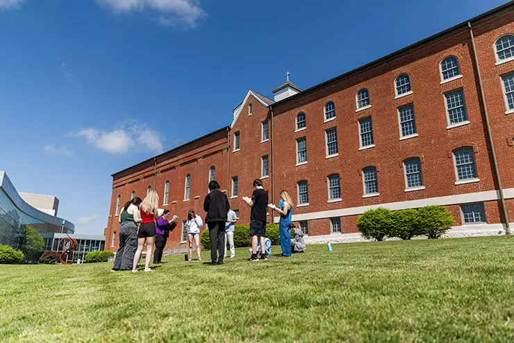 a group of students stand together on the lawn outside of the River Campus Seminary building