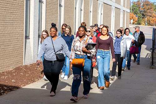 a group of students and parents walking beside a campus building during a Show me Day college visit tour