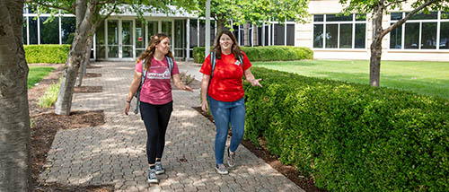 two southeast missouri state university students walk across campus under shade trees with bright green grass around them