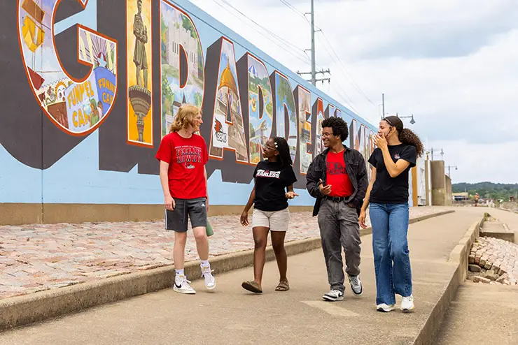a group of SEMO students walks along the river floodwall with the cape girardeau mural painted on it
