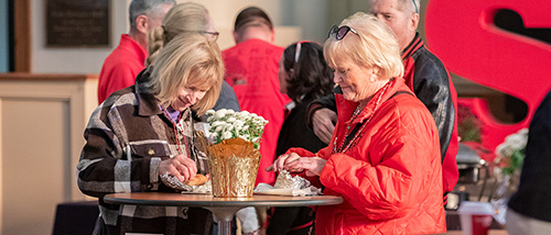 On the morning of Homecoming, two alumni stand at a table eating at the annual Alumni Breakfast.