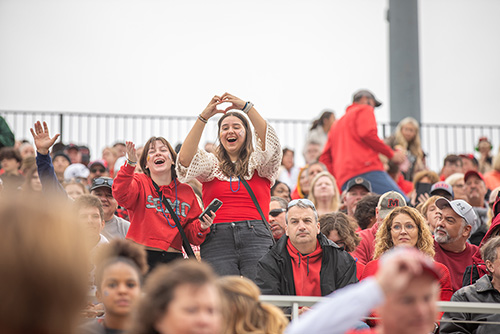 Two girls stand on the bleachers sporting face paint and making hearts with their hands.