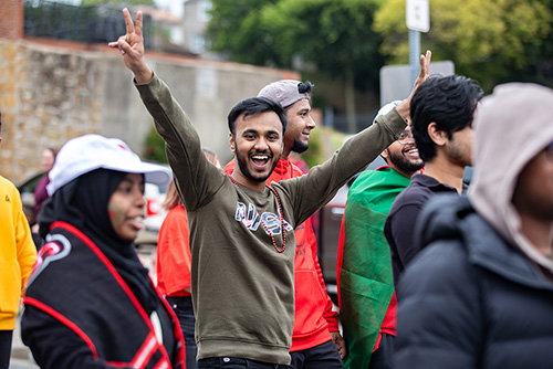 A man stand in the middle of a group with both arms out sporting peace signs