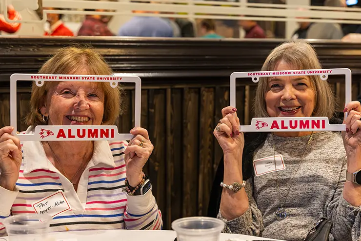 Two ladies holding up SEMO alumni license plates and smiling