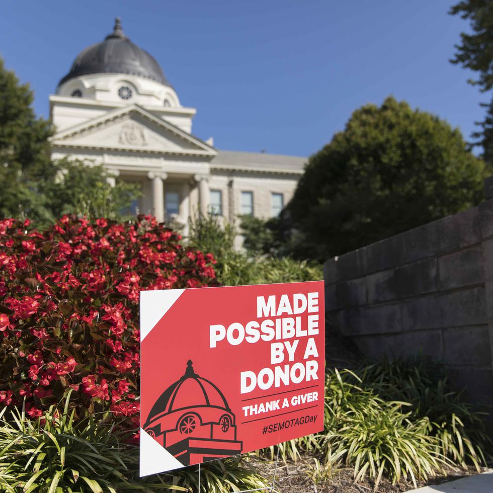 A sign reading “MADE POSSIBLE BY A DONOR” sits in colorful landscaping in front of Academic Hall. 