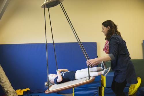 A staff member at the University Autism Center pushes a child on an indoor platform swing.