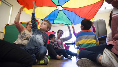 Staff members and children play with a parachute inside at the University Autism Center.