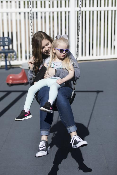 A staff member holds a child as they swing on the playground outside at the Autism Center.