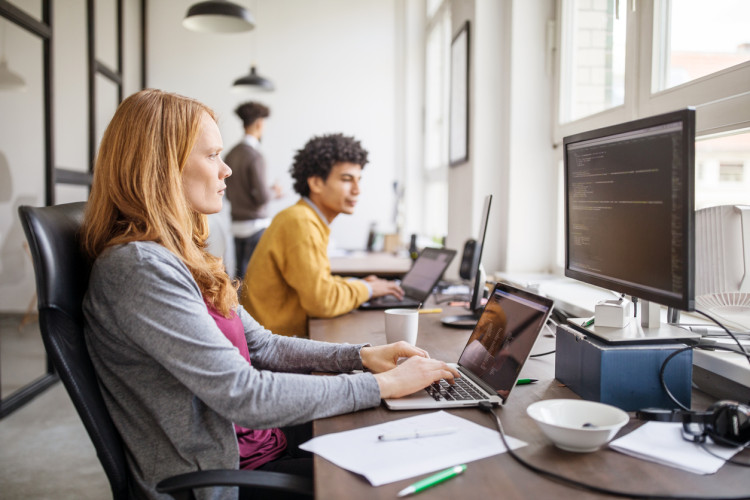 A tech professional sitting in front of a computer in a row of desks with co-workers.