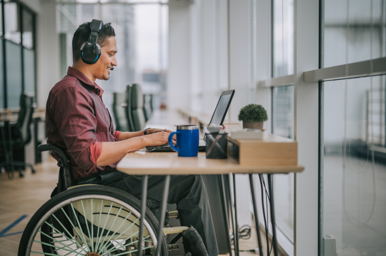 A student sitting at a desk in a wheelchair with headphones on.