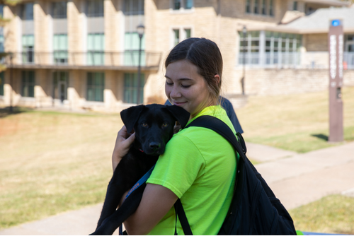 A student holds a black puppy near Academic Hall.
