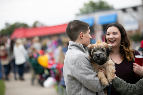 A person holds a dog during the SEMO Homecoming Parade as they talk to a friend.