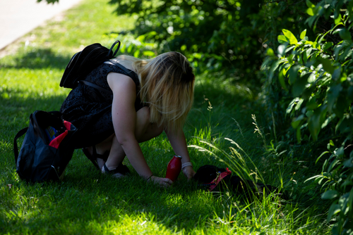 A student kneels in the grass to give their dog water on a hot day.