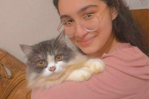 A student holds a gray and white cat and smiles at the camera.
