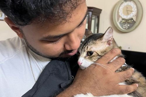 A student cuddles a small cat to his chest.