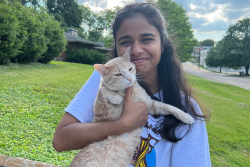 A student cuddles an orange cat with one arm outside on the SEMO campus.