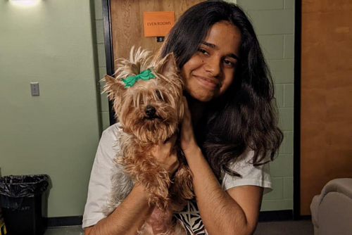 A SEMO student smiles and holds up a small brown and black dog to the camera.