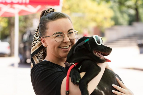 A female student with glasses smiles while holding a black dog tightly