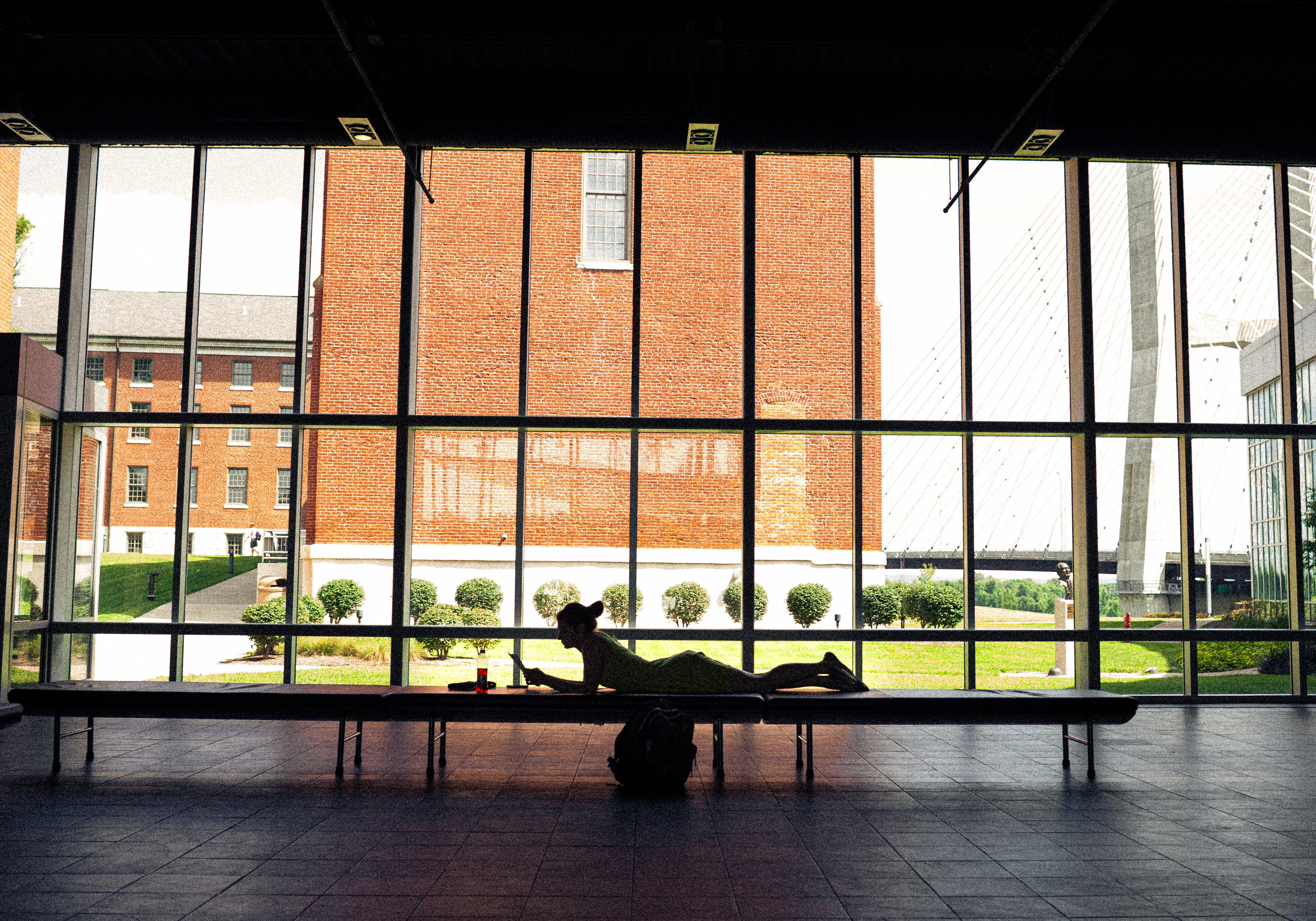 A college student laying on a bench doing homework on a laptop in the Cultural Arts Center in front of the windows overlooking River Campus at Southeast Missouri State University.